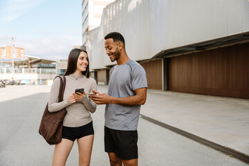 Female athlete listening to male athlete while they stand and smile while holding phones