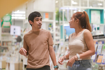 Fototapeta premium A couple walking through a brightly lit aisle of bookshelves (likely a bookstore or mall library). The man points toward the shelves as he speaks to the woman.