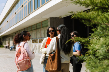 A group of four female students stand while two of them talk and two of them listen while holding...