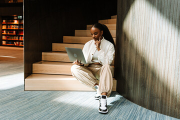 Fototapeta premium Female student looking at laptop while sitting on stairs