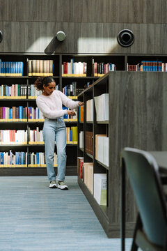 Female student walking and looking for a book on a bookshelf
