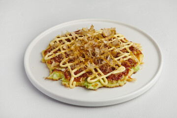 Okonomiyaki with mayo and bonito flakes on white plate, selective focus