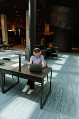Female student looking at laptop and listening to headphones while sitting on chair at desk