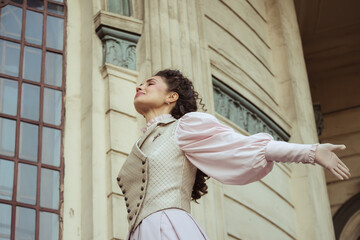 Fototapeta premium An elegant woman in a vintage dress stands by an old stone column