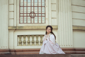 Fototapeta premium An elegant woman in a vintage dress stands by an old stone column