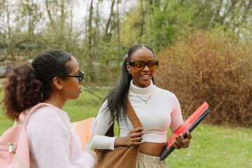 Female student smiling and looking away while holding folders and talking to female student holding notebooks