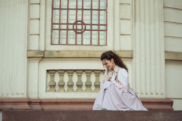 Fototapeta premium An elegant woman in a vintage dress stands by an old stone column