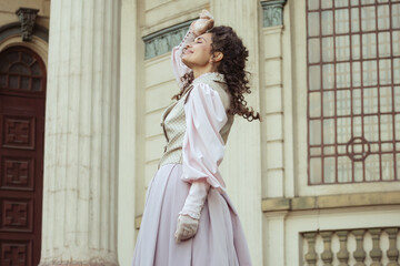 Fototapeta premium An elegant woman in a vintage dress stands by an old stone column