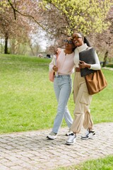 A female student hugs a female student walking next to her while they laugh and hold notebooks and...