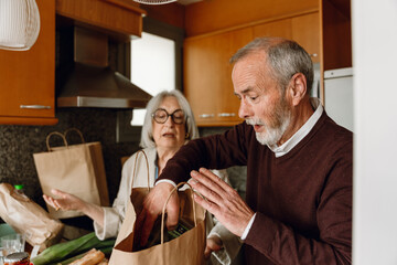 A man takes groceries out of a bag while talking to a woman standing next to him