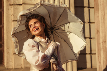 An elegant woman in a vintage dress holds a lace parasol under the warm rays of the sun.