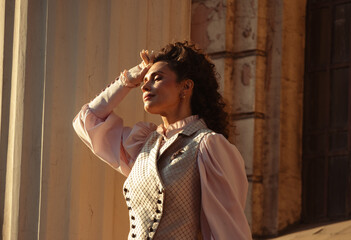 Fototapeta premium An elegant woman in a vintage dress stands by an old stone column