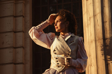 Fototapeta premium Portrait of a woman in vintage clothing, illuminated by warm sunlight, against a backdrop of ancient architecture.