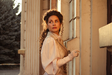 Fototapeta premium Portrait of a woman in vintage clothing, illuminated by warm sunlight, against a backdrop of ancient architecture.