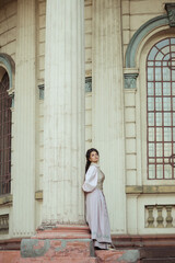 Fototapeta premium An elegant woman in a vintage dress stands by an old stone column