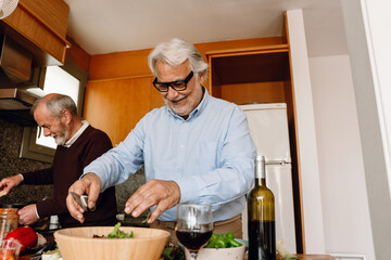 A man holds a knife over a bowl while his friend stands next to him and they laugh