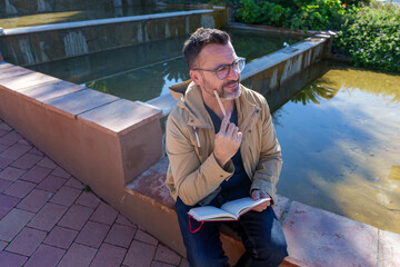 Man thinking outdoors holding notebook and pencil, contemplating creative ideas for writing and planning