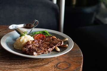 Freshly grilled steak served with mashed potatoes, roasted tomato, green beans, and brown gravy on a rustic wooden table. Perfect for restaurant promotions, menu design, editorial food content