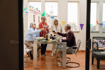 A group of four friends laughing and talking while holding glasses while two of them are standing...