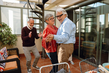 A man and a woman are dancing and smiling while holding hands and a male friend is standing next to them and applauding
