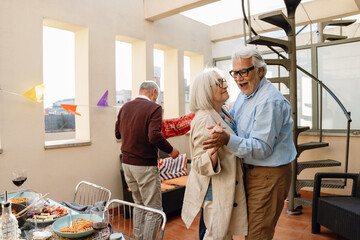 A man is talking to a woman with whom he is holding hands and dancing while smiling and a male friend is standing next to them