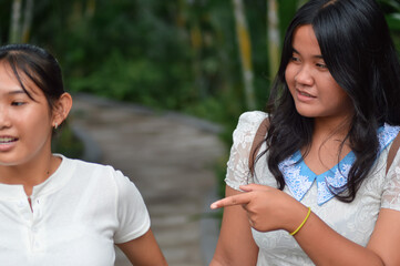 A close-up of two teenage girls walking together along a garden path. One in a lace top points off-camera while talking to her friend in a henley top, possibly deciding where to rest.