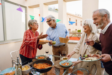 Group of four friends talking and laughing while standing at a table and holding plates and a glass