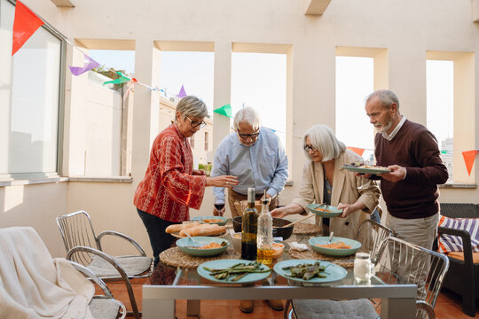 A group of four friends standing at a table while holding plates and bowls - Powered by Adobe
