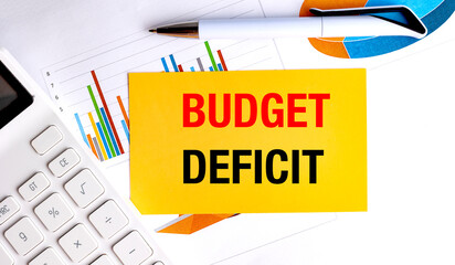 Budget deficit concept on yellow paper with charts, pen, and calculator on white office desk
