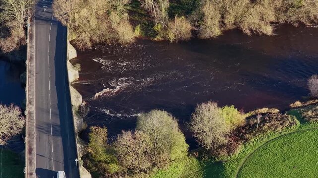 Aerial drone footage of the town of Ripon in North Yorkshire in the UK showing traffic going over the main road and bridge going over a River Ure in the winter time with trees on either side