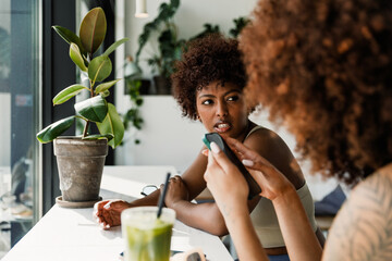 A woman is talking to a female friend who is looking at her phone while they are sitting at a table