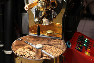A modern coffee roasting machine filled with brown coffee beans stands next to a control panel with colorful buttons. The professional setup enables precise roasting and flavor control.