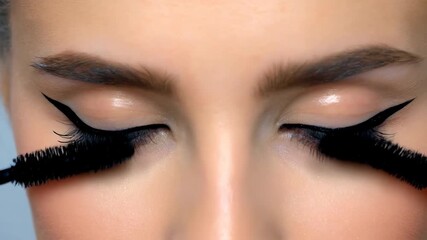 Close-Up Video Of A Young Woman Applying Black Mascara And Blinking Her Blue Eyes.
