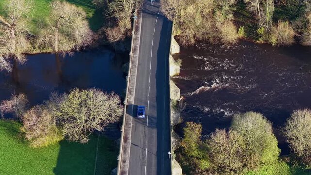 Aerial drone footage of the town of Ripon in North Yorkshire in the UK showing traffic going over the main road and bridge going over a River Ure in the winter time with trees on either side
