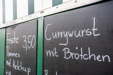 A chalkboard menu lists popular food items, specifically highlighting currywurst, inviting food lovers to indulge in delicious local culinary delights.