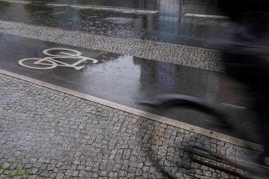 This photo captures a wet street reflecting droplets of rain, with clear bicycle path markings, symbolizing motion and daily life amidst changing weather conditions.