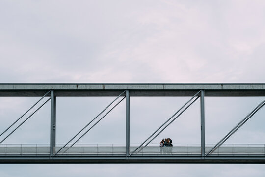 A group of people stands together on a modern bridge structure, set against a cloudy sky, capturing urban life and how people connect in public spaces.