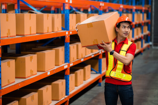A man wearing a safety vest is holding a box in a warehouse