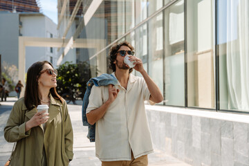 Fototapeta premium A man drinks while walking next to a woman who is talking and smiling as they hold cups