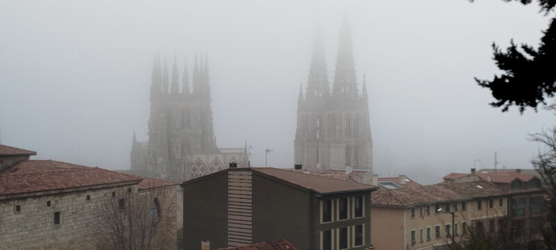 Torres g&oacute;ticas de Catedral de Burgos, entre niebla con tejados y &aacute;rboles en primer plano