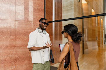 A male employee gestures and talks to a female employee standing across from him while they hold folders
