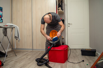 A man is focused on performing maintenance on a vacuum cleaner in a home setting, likely changing...