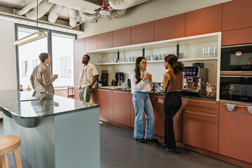 Two female workers are standing next to two male workers and they are talking while two of them are holding cups