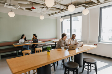 A group of four workers sit at tables in pairs and talk