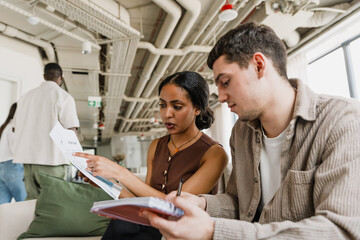 A female employee is talking and pointing at a document while a male employee is sitting next to...