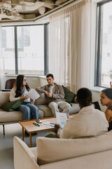 Fototapeta premium A group of four employees sit on sofas at a table and talk while two of them hold documents