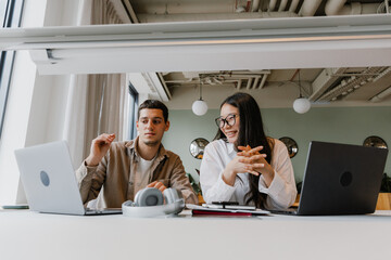 Male and female workers looking at laptop and sitting at table while she laughs