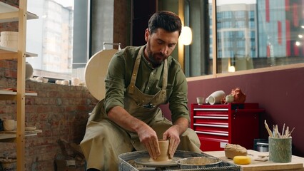 Caucasian craftsman man male guy businessman potter small business owner wet hands water work with clay material brown mud pottery shaping molding stoneware manufacturing hobby indoor workshop studio