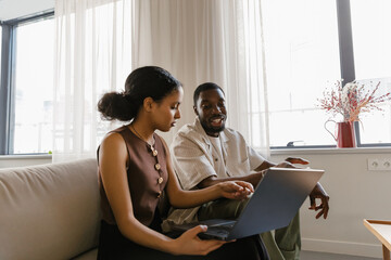 Male worker talking and pointing at laptop being shown to him by female worker while they sit on...