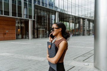 Fototapeta premium Female worker holding a folder and talking on the phone while standing and looking in front of her